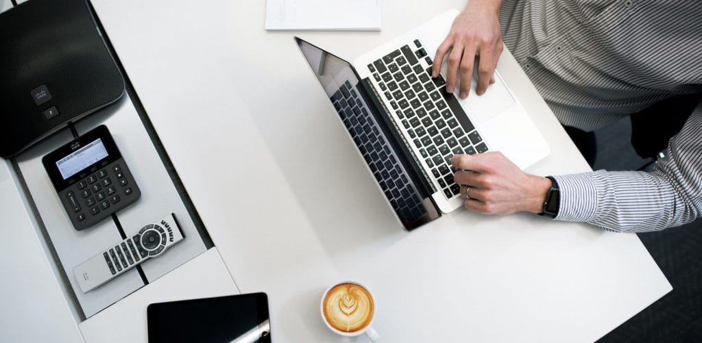 View from above of a laptop, a phone and a coffee on a white desk