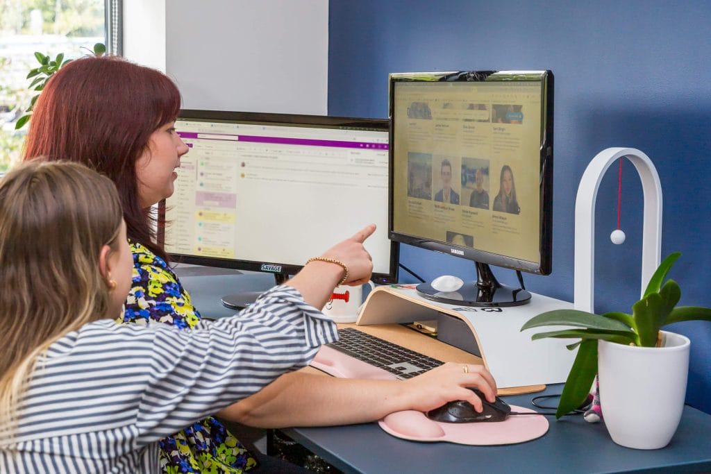 Two team members sitting at a desk, talking and working on a computer in Unbranded Digital office