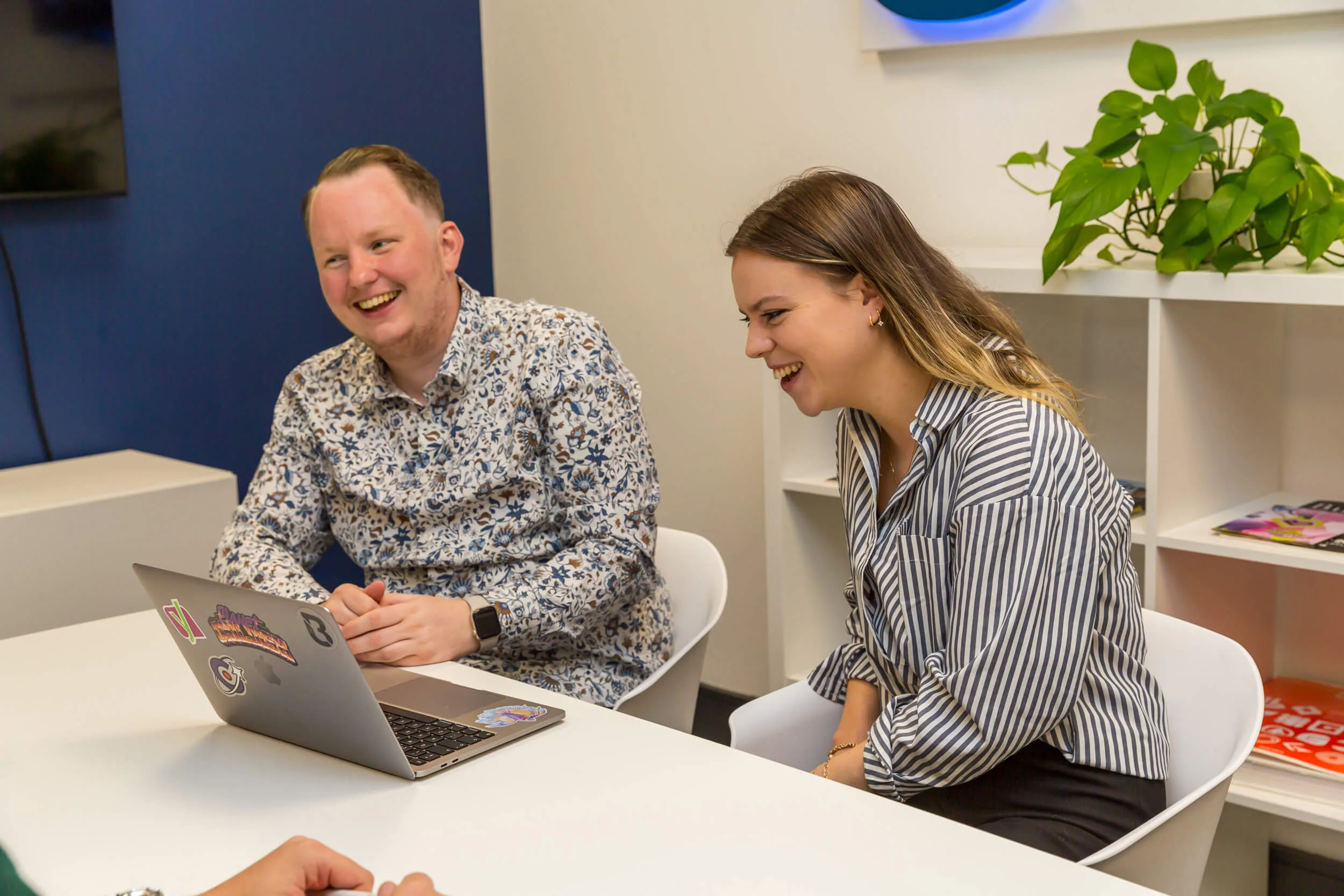 Two team members sitting at a desk and working on a laptop in a meeting room