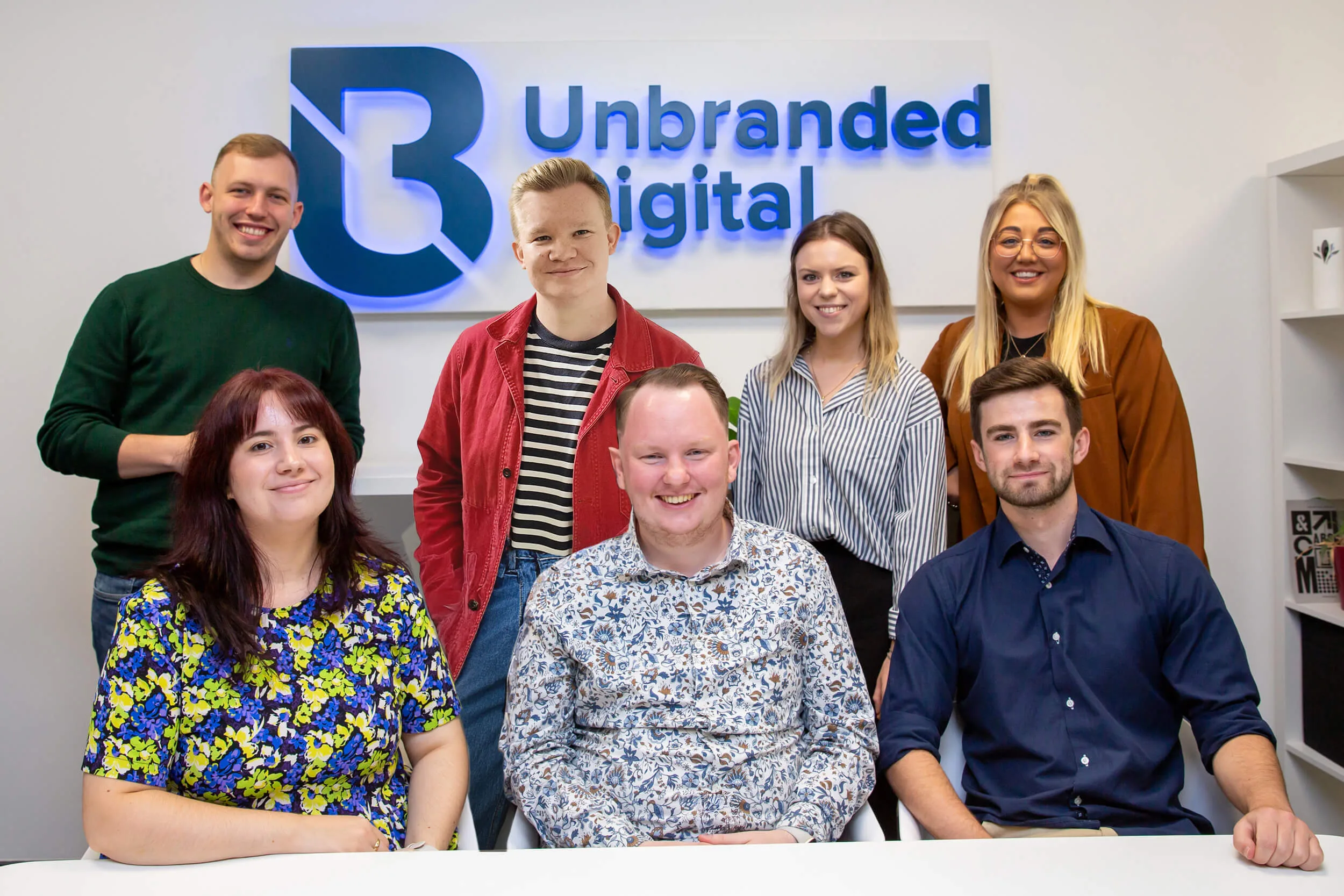Unbranded Digital Team in the office in front of the Unbranded Digital sign